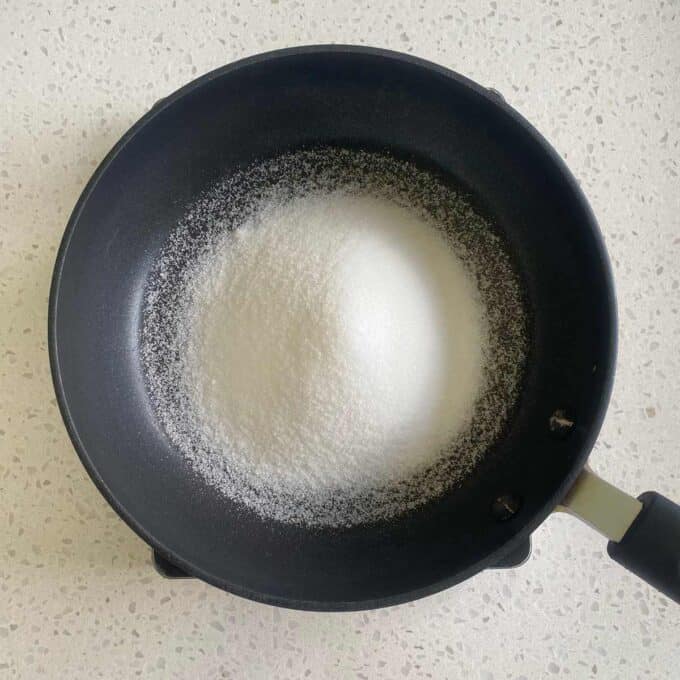 A black pan filled with white sugar is placed on a speckled countertop.
