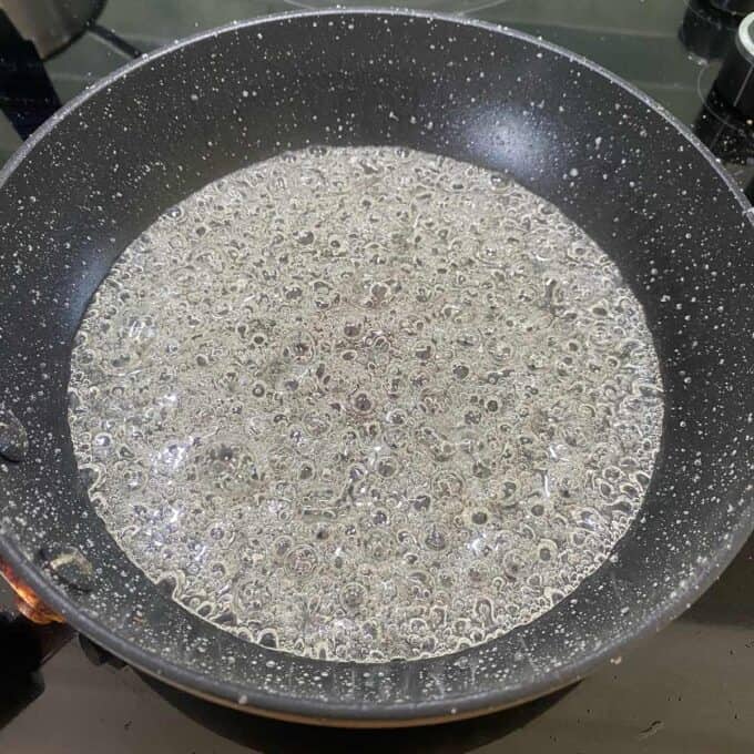 A frying pan filled with bubbling water on a stove.