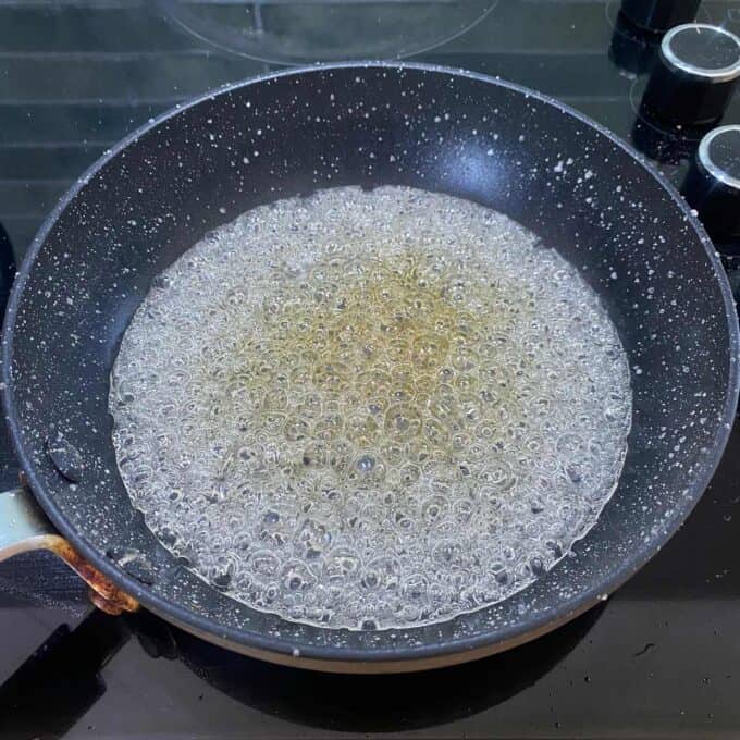 A non-stick frying pan on a stove with bubbling hot sugar syrup inside.