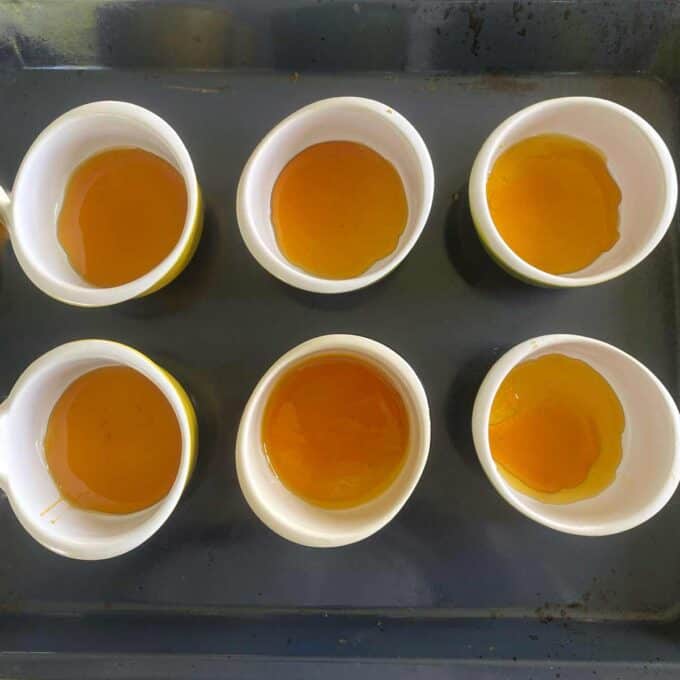 Six white bowls filled with a golden liquid, evenly spaced on a dark surface.