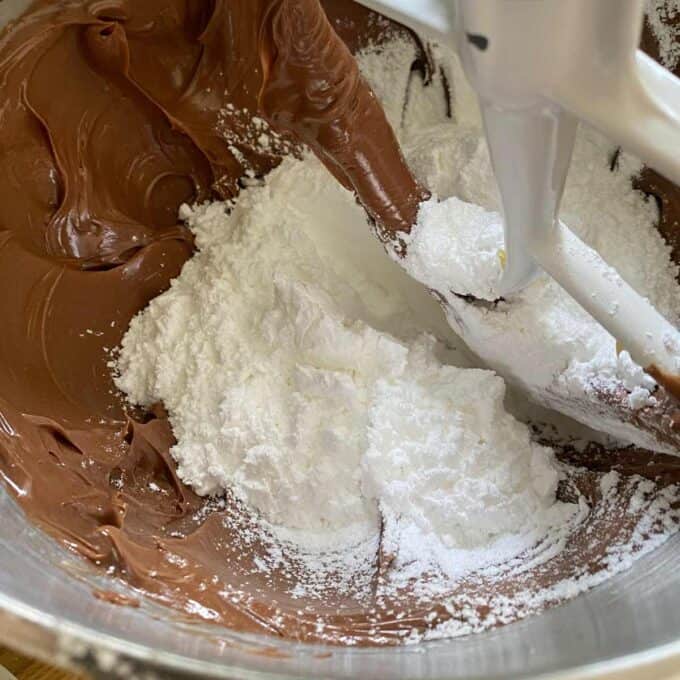Mixer blade in a bowl with chocolate and white powdered sugar being combined.