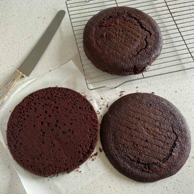 Two chocolate cakes sliced in half on a white bench top.