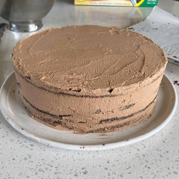 A chocolate cake covered in buttercream icing on a white plate.