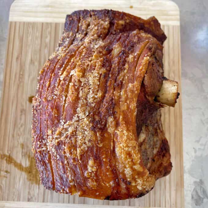Roasted pork with crispy, golden skin rests on a wooden cutting board.