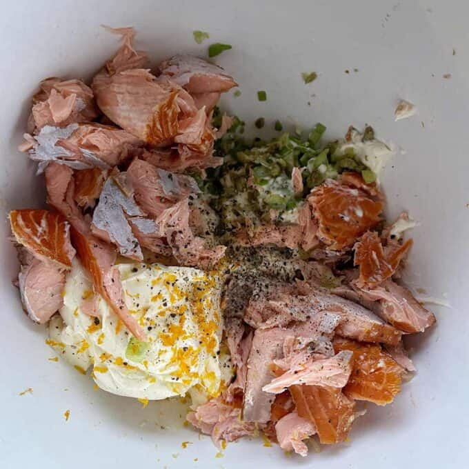 Bowl containing flaked salmon, mayonnaise, chopped green onions, and spices.
