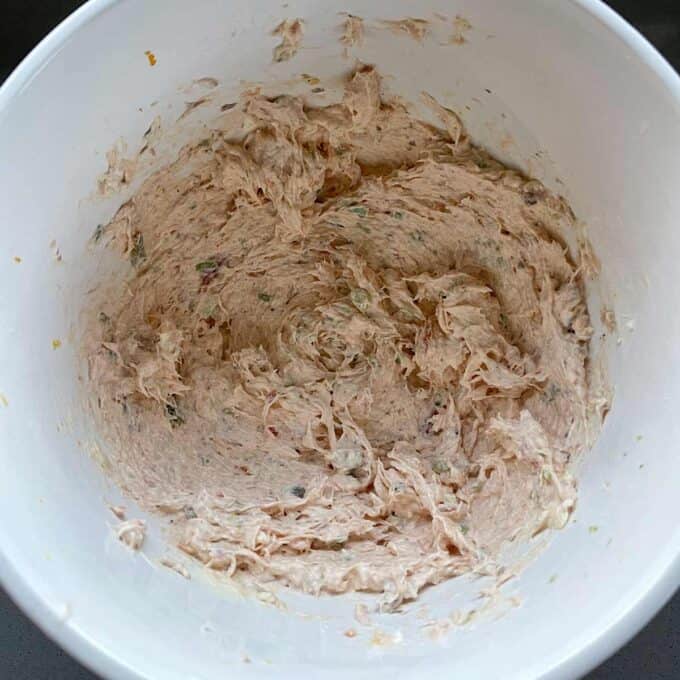 A white bowl containing a mixed, creamy spread with visible flecks of herbs and spices.