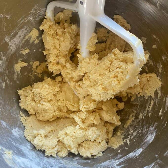 Cookie dough in a metal mixing bowl with a white paddle attachment.