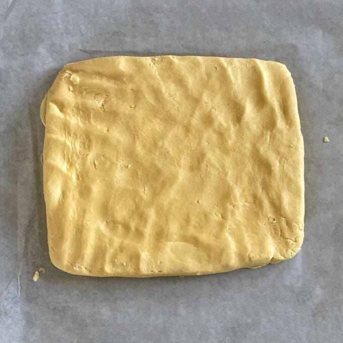 A rectangular block of dough rests on a piece of parchment paper.