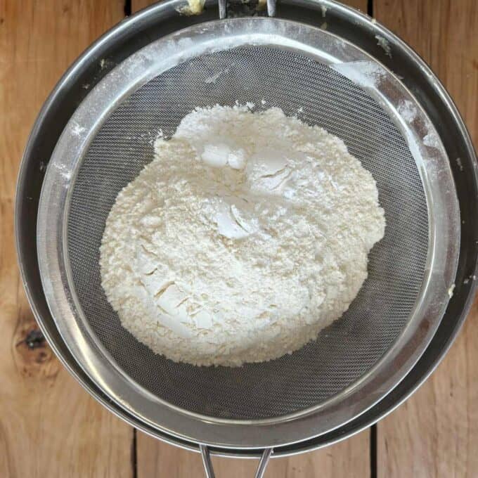 Flour in a fine sieve placed over a wooden surface, ready for sifting.