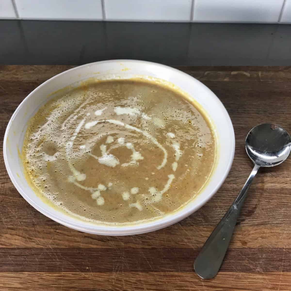 Slow Cooker Whole Chicken Soup A bowl of creamy soup with a swirl of cream on top sits on a wooden surface next to a metal spoon.