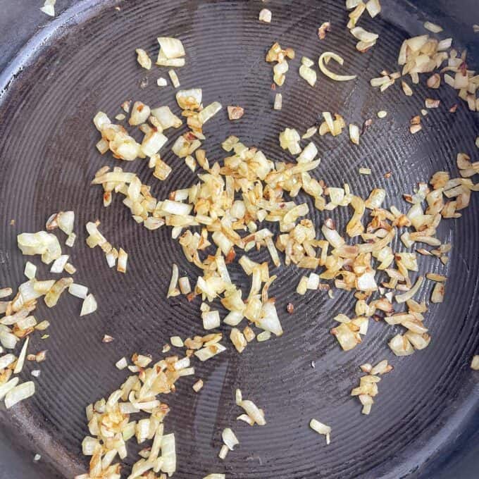 Chopped onions being sautéed in a frying pan until golden brown.