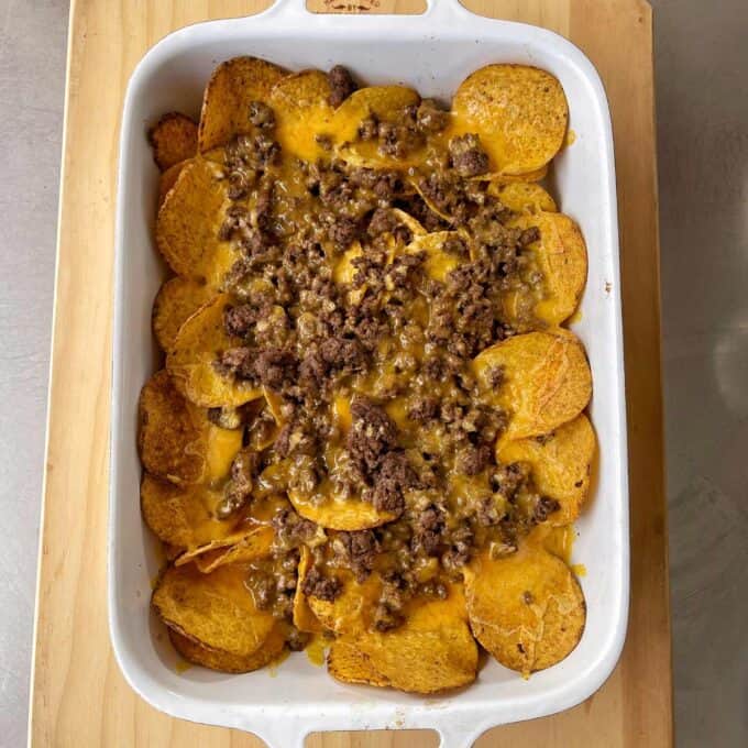 A white baking dish filled with nachos topped with melted cheese and ground beef on a wooden surface.
