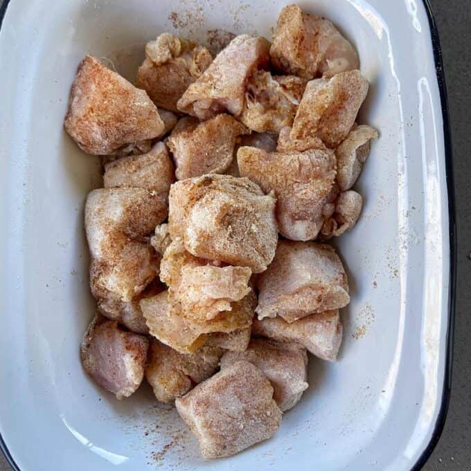 Raw, seasoned chunks of frozen chicken placed in a white rectangular dish with a black rim.