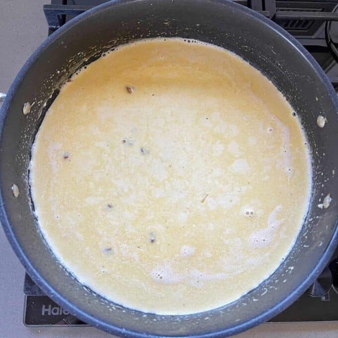 A pot of light yellow sauce or soup simmering on a stovetop, with some small chunks visible in the liquid.