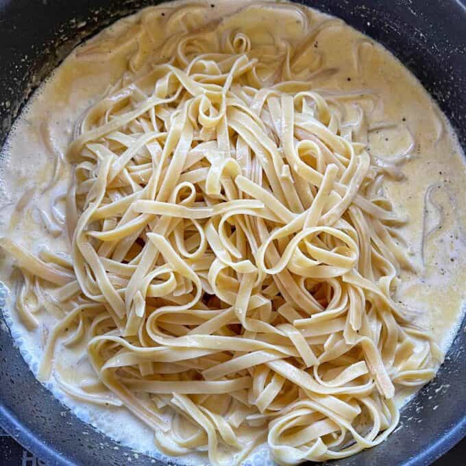 A pan filled with cooked fettuccine pasta in a creamy white sauce.