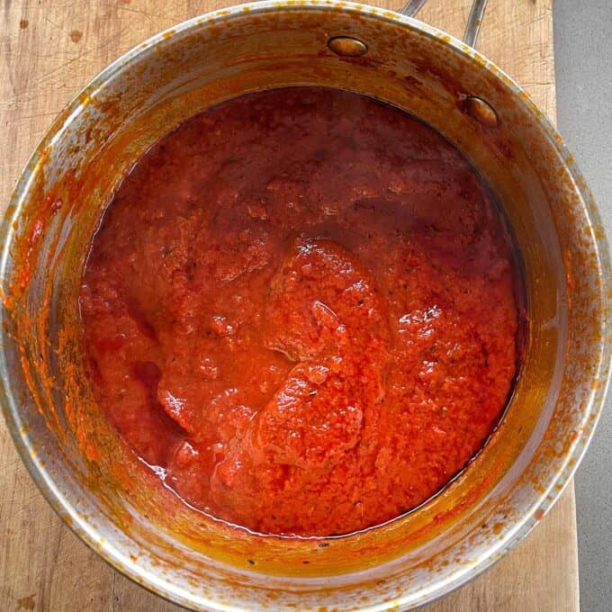 A metal pot filled with red tomato sauce sits on a wooden surface.