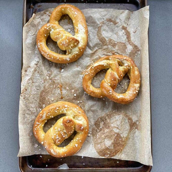Three salted pretzels on a parchment-lined baking sheet.