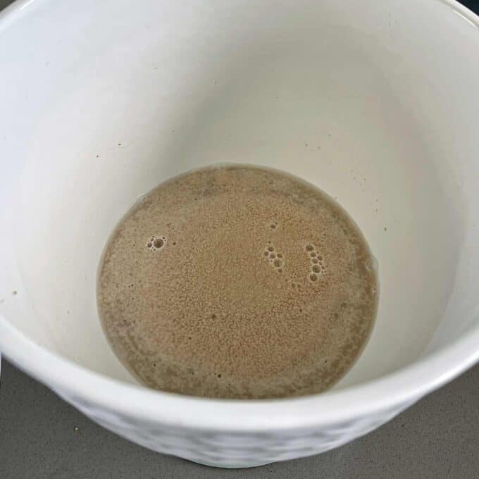 A white bowl containing a mixture of activated yeast and liquid, with foam and bubbles visible on the surface.