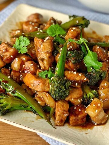 A plate of stir-fried chicken with broccoli in a brown sauce, garnished with sesame seeds and fresh cilantro.