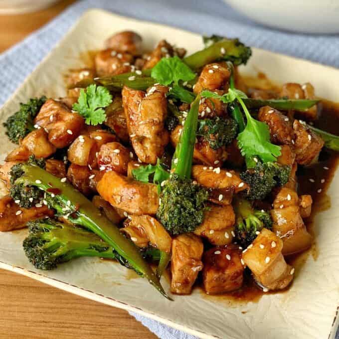 A plate of stir-fried chicken with broccoli in a brown sauce, garnished with sesame seeds and fresh cilantro.