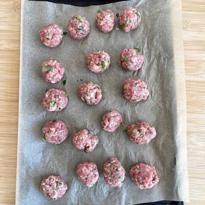 Raw meatballs arranged in rows on a parchment-lined baking sheet, ready to be cooked.