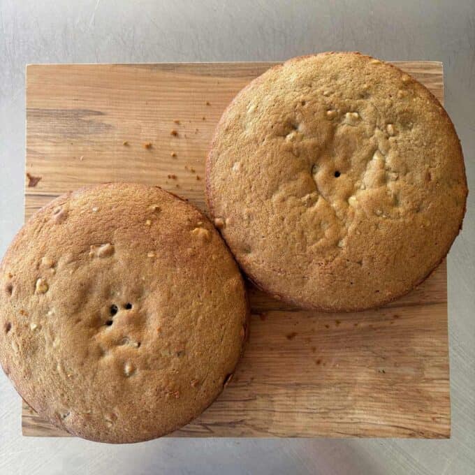 Two round, golden-brown cakes with small holes on top, placed side by side on a wooden board.