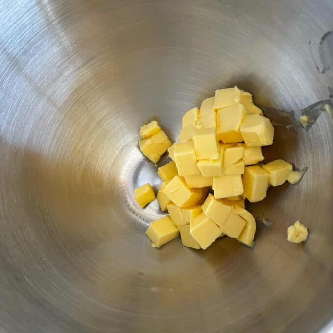 Cubed pieces of butter in the bottom of a large stainless steel mixing bowl.