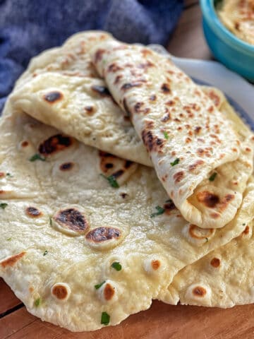 Three pieces of homemade flatbread with browned spots and green herb flecks on a white plate, next to a blue bowl of dip.