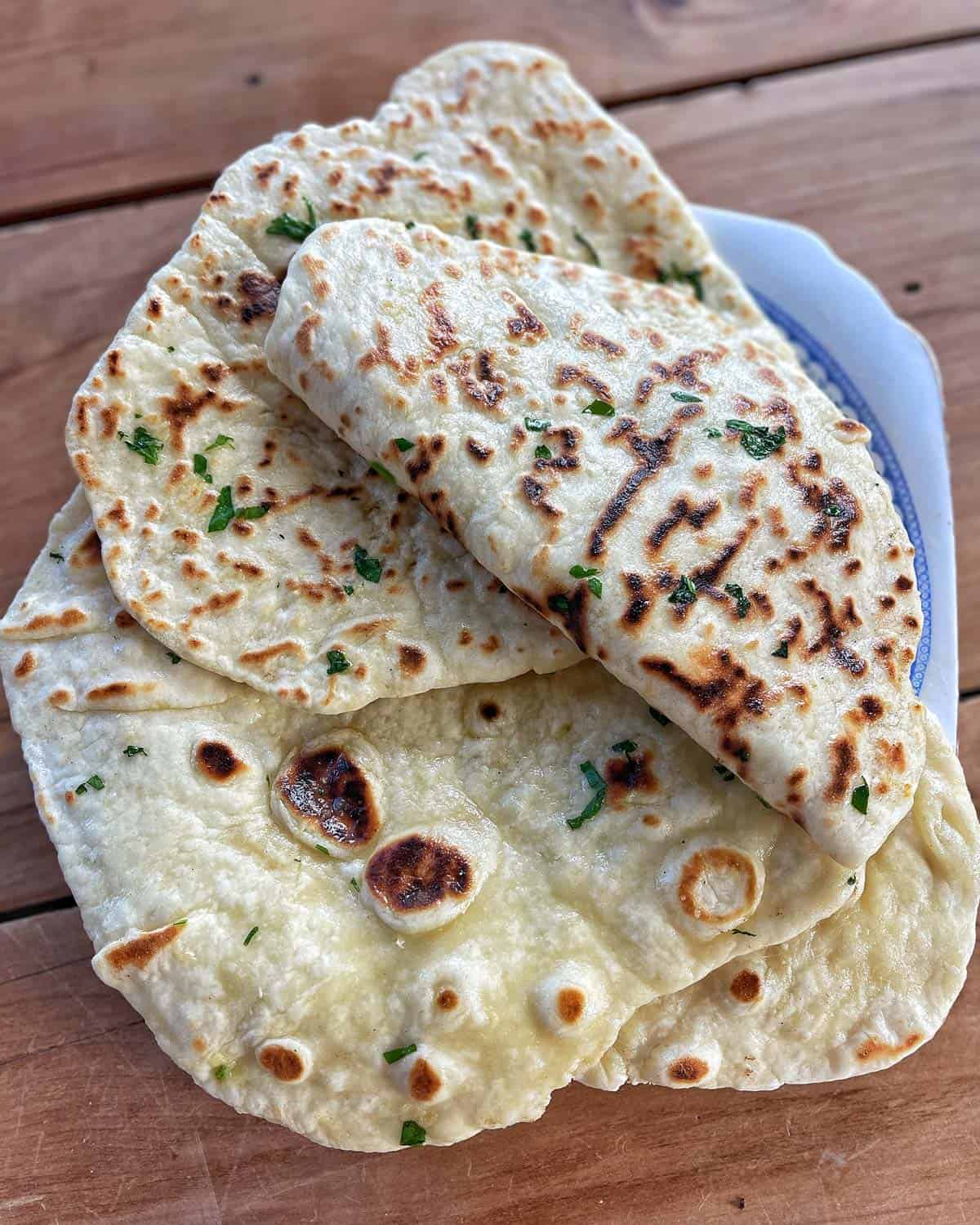 Flatbreads Three pieces of flatbread with green herbs are stacked on a plate set on a wooden surface.