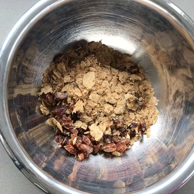 A stainless steel bowl containing a mixture of chopped dates and nutritional yeast flakes.