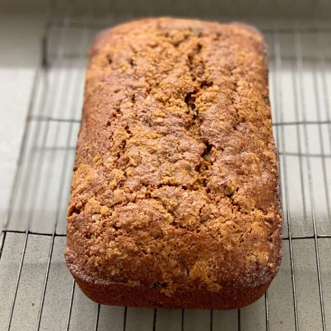 A loaf of golden-brown bread with a cracked top is cooling on a wire rack.