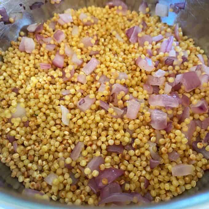 A close-up of cooked quinoa mixed with diced red onions in a metal bowl.