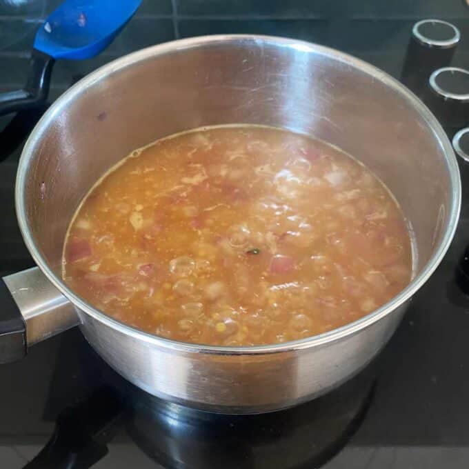 A stainless steel pot containing a simmering mixture of diced ingredients in a brownish liquid on a stovetop.