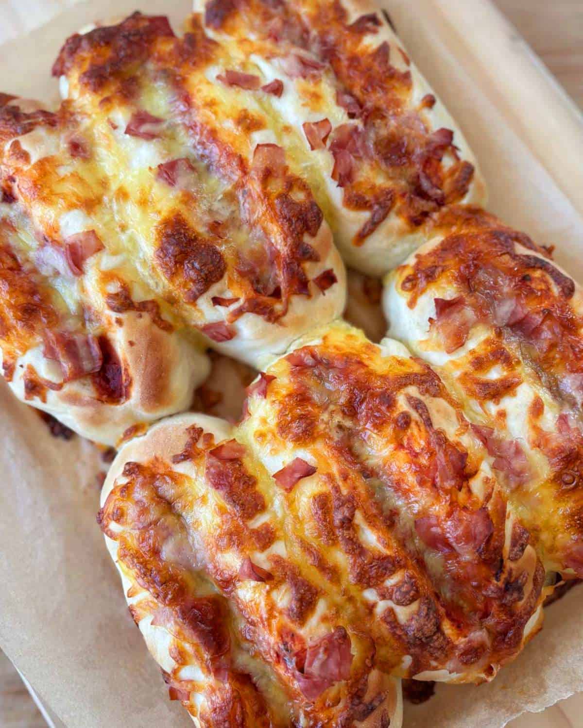 Pizza Rolls Four baked cheesy bread loaves topped with melted cheese and diced ham, arranged on parchment paper.