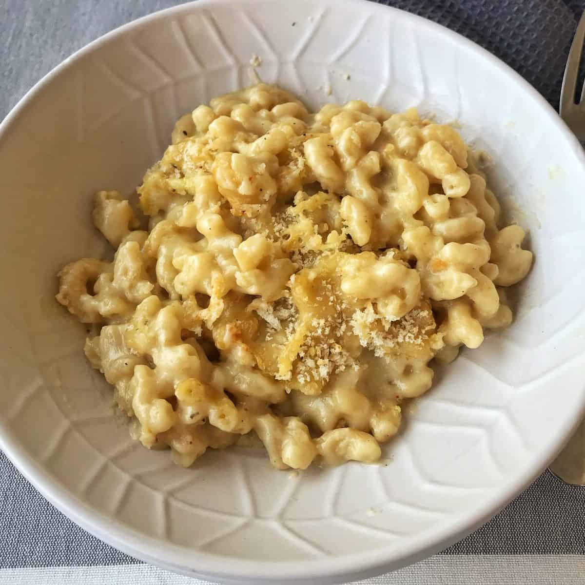 Slow Cooker Mac and Cheese A white bowl filled with baked macaroni and cheese topped with breadcrumbs, placed on a gray and white tablecloth.