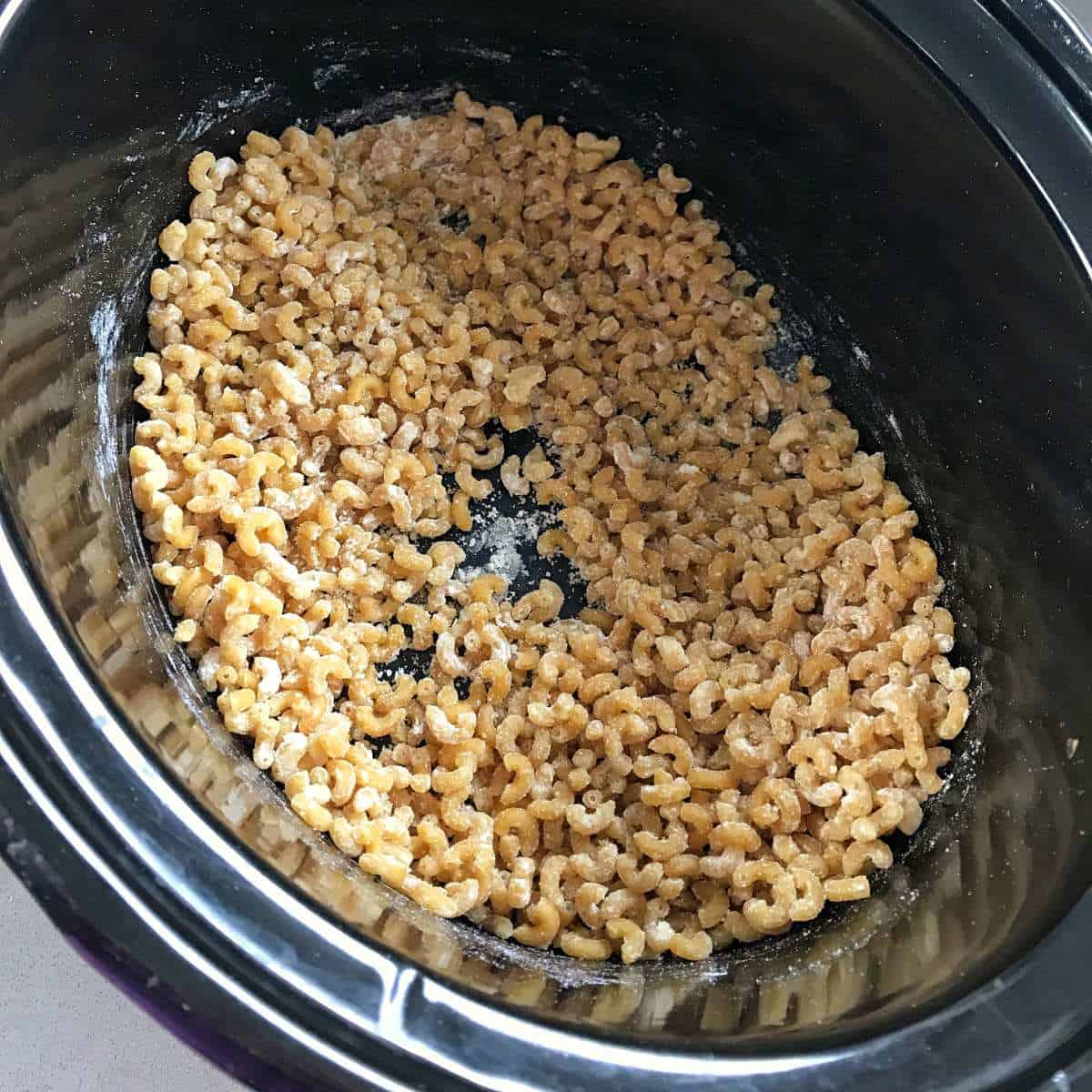 Slow Cooker Mac and Cheese Uncooked macaroni noodles coated with powder sit at the bottom of a black slow cooker.