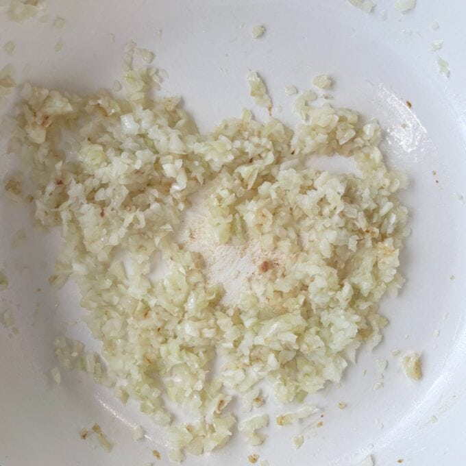 Homemade Baked Beans Finely chopped onions sautéing in a white pan, starting to turn translucent with slight browning at the edges.