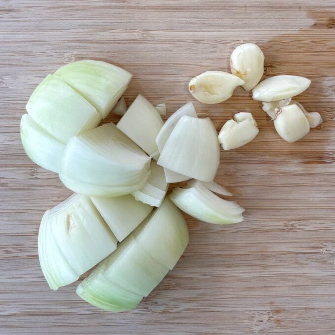 Homemade Baked Beans Chopped white onion and peeled garlic cloves on a wooden cutting board.