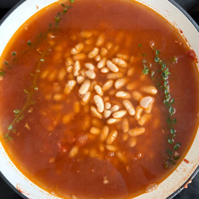 Homemade Baked Beans A pot of white beans in tomato sauce with sprigs of fresh thyme on top.