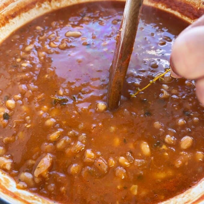 Homemade Baked Beans Close-up of a pot of baked beans in a thick, reddish-brown sauce being stirred with a spoon.