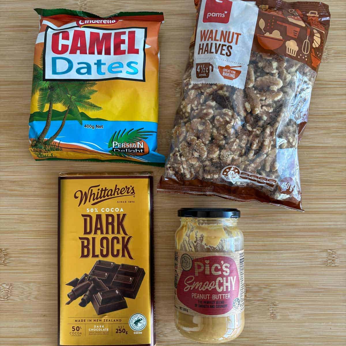 Date and Chocolate Bark A bag of Camel dates, a bag of Pam’s walnut halves, a Whittaker’s dark chocolate bar, and a jar of Pic’s smooth peanut butter on a wooden surface.