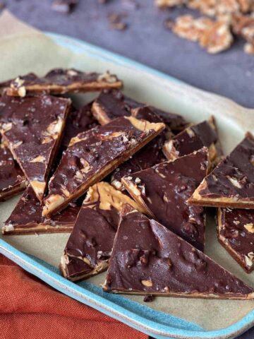 A tray of triangular chocolate bark pieces with visible layers of chocolate, caramel, and nuts, arranged on parchment paper.