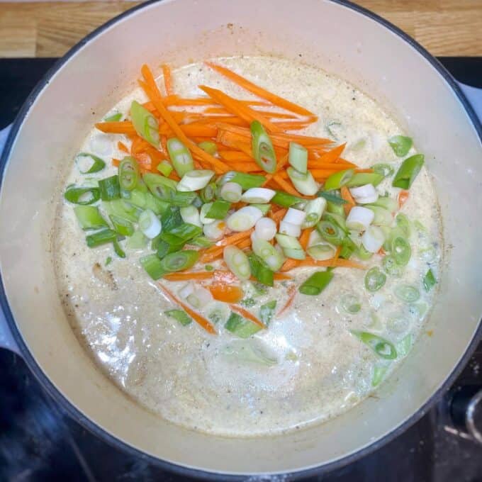 Dixie Chicken A pot of creamy soup is cooking on a stovetop, topped with sliced carrots and chopped green onions.
