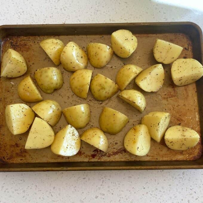 Dixie Chicken Quartered potatoes seasoned with pepper and oil, arranged on a baking sheet, ready to be roasted.