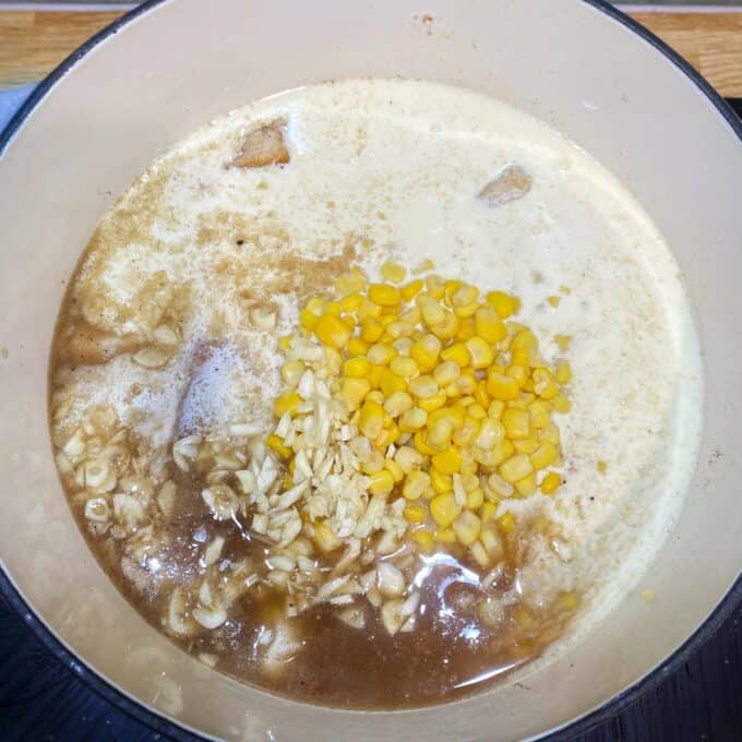 Dixie Chicken A pot with broth, cream, corn kernels, chopped garlic, and chicken pieces being prepared on a stove.