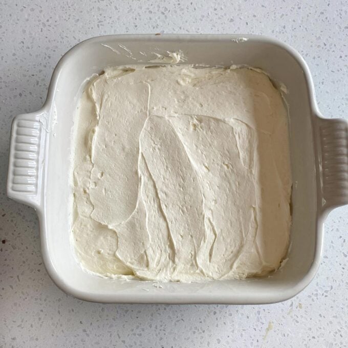 Square ceramic dish filled with an even layer of smooth, creamy batter on a light speckled countertop.