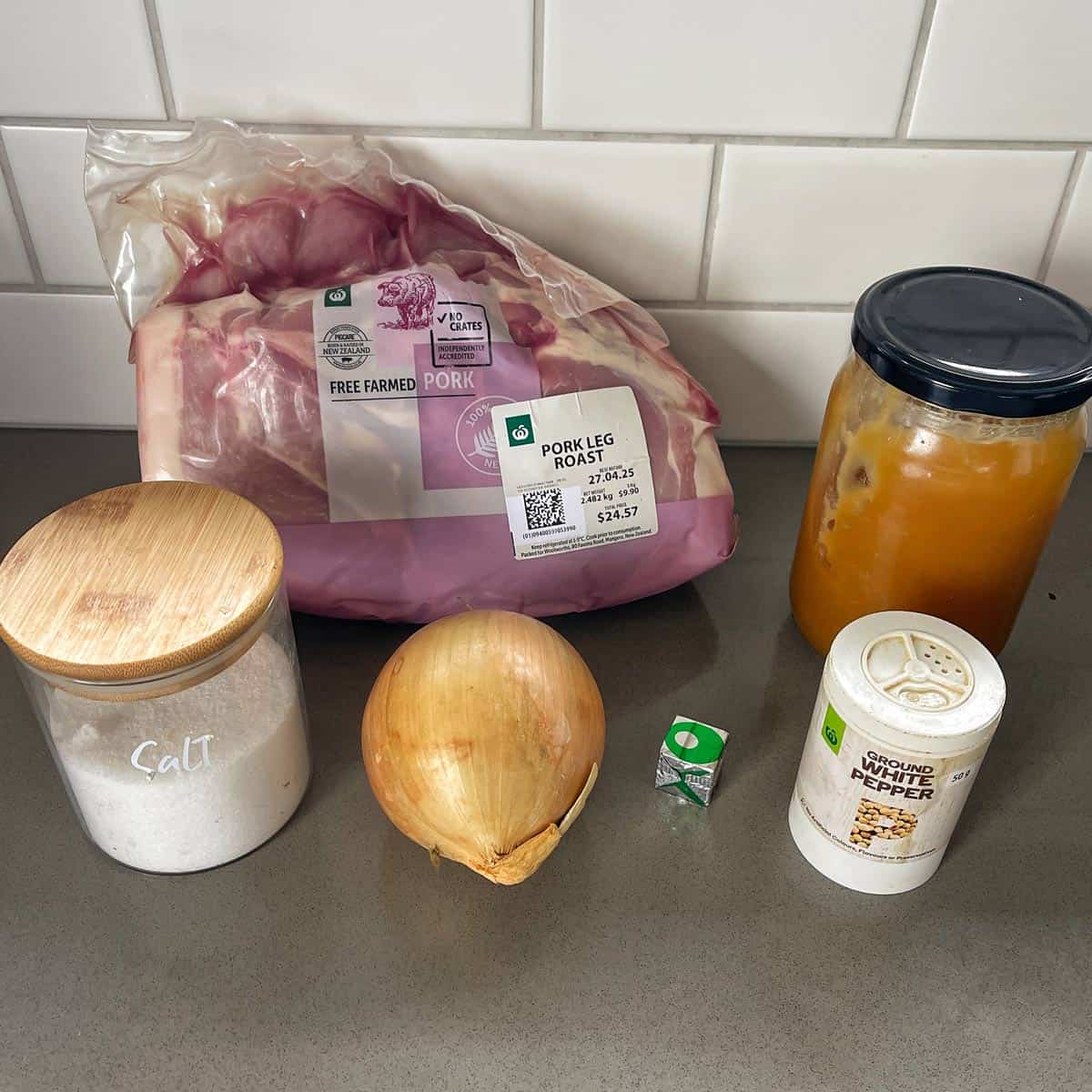 Slow Cooker Honey Pork A pork leg roast, jar of brown liquid, container of salt, onion, bouillon cube, and white pepper shaker on a gray countertop.