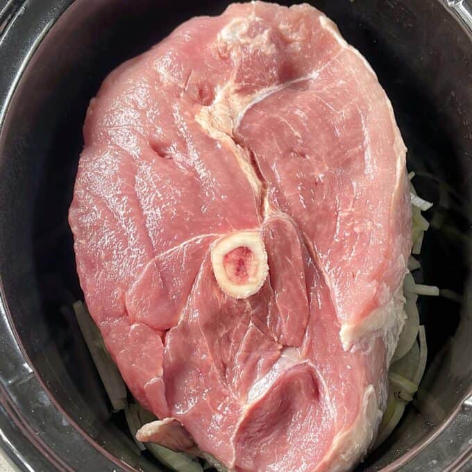 Slow Cooker Honey Pork A raw ham steak with a bone in the center placed inside a black slow cooker.