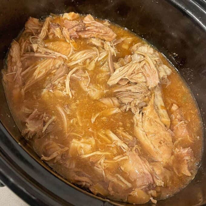 Slow Cooker Honey Pork Shredded cooked meat in a brown broth inside a slow cooker.