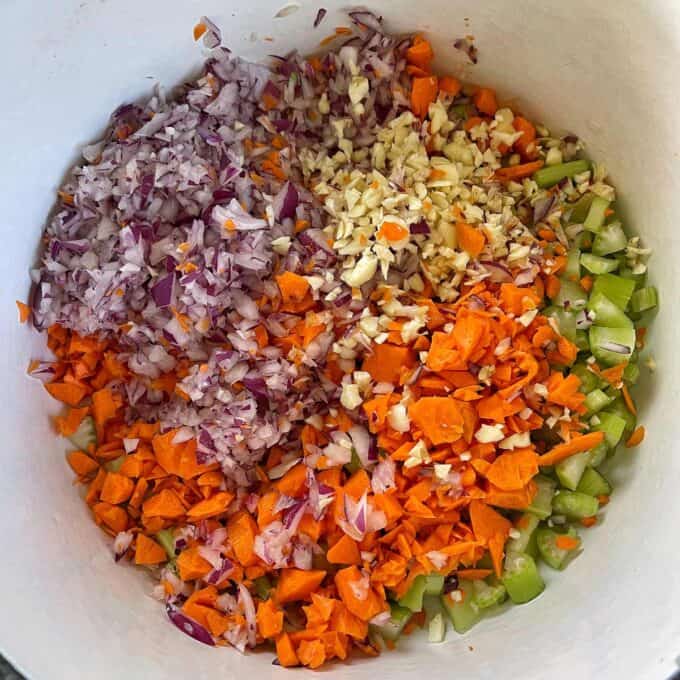 Caponata Chopped red onion, garlic, carrots, and celery are arranged in sections inside a white mixing bowl.